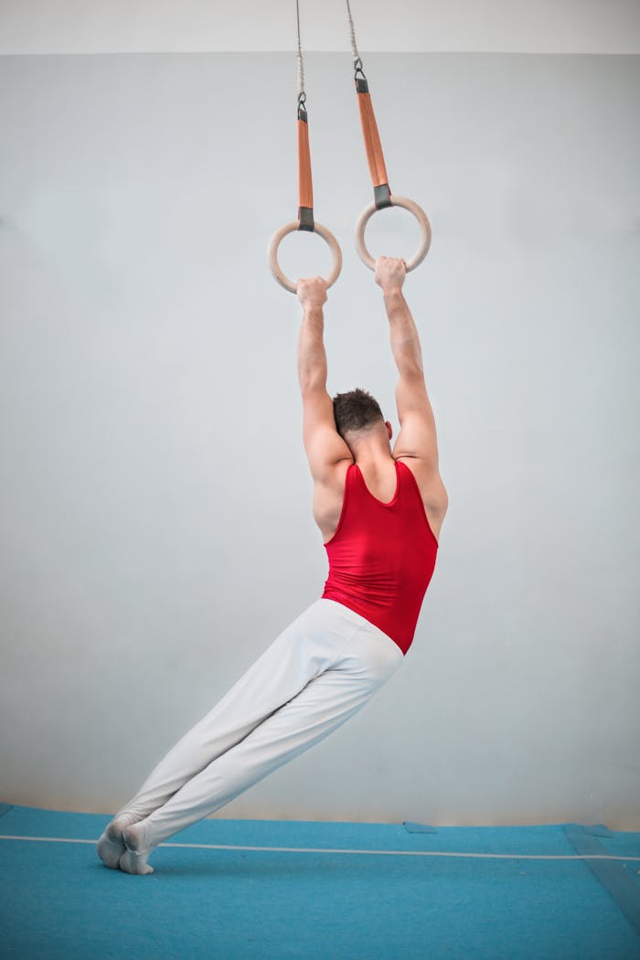 gallery-03 A male gymnast displaying strength and balance on rings inside a gym setting.