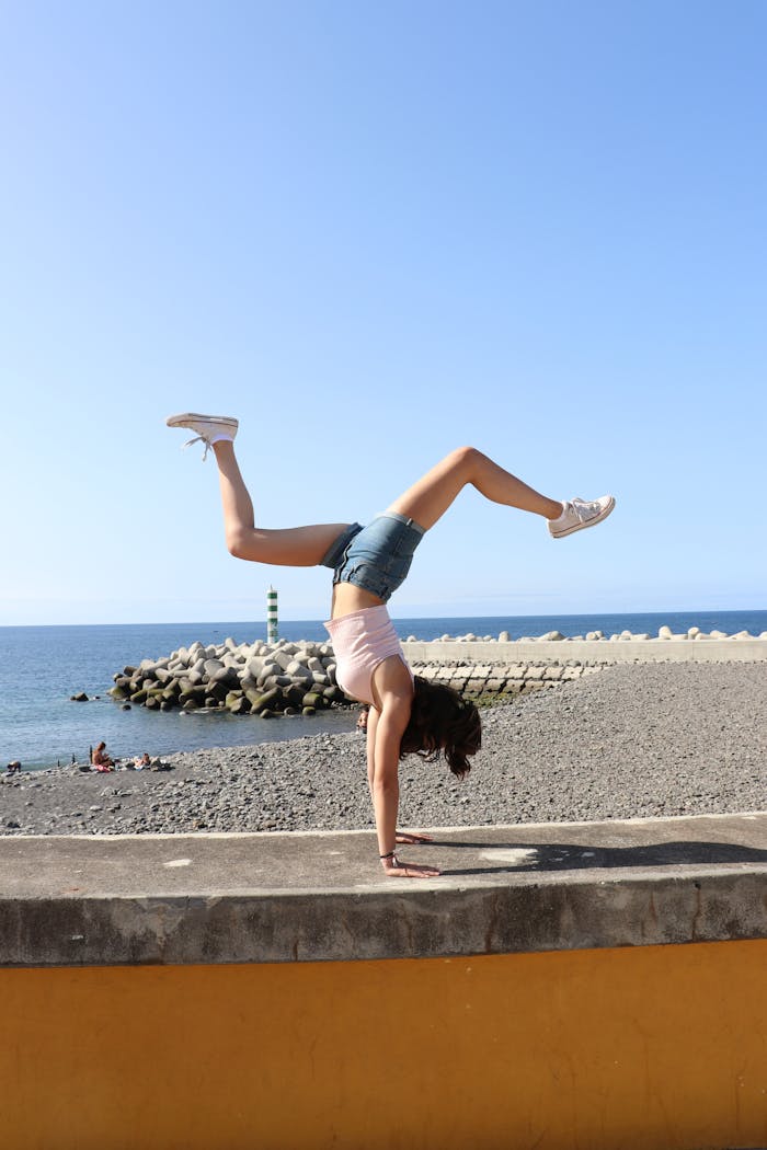 A fit woman doing a handstand on a sunny day at Madeira beach, showcasing strength and flexibility.