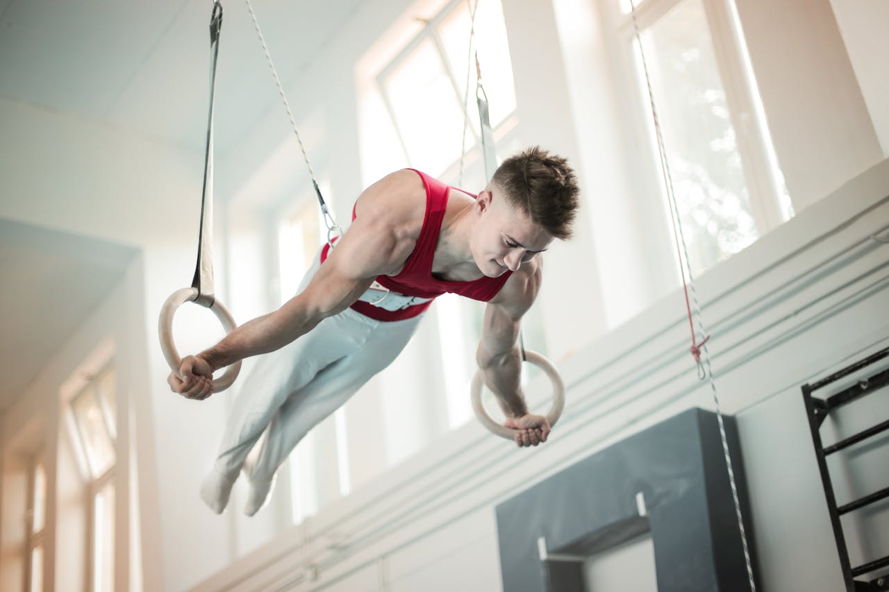 about-us-01 A male gymnast showcases strength and balance on rings during practice inside a gym.